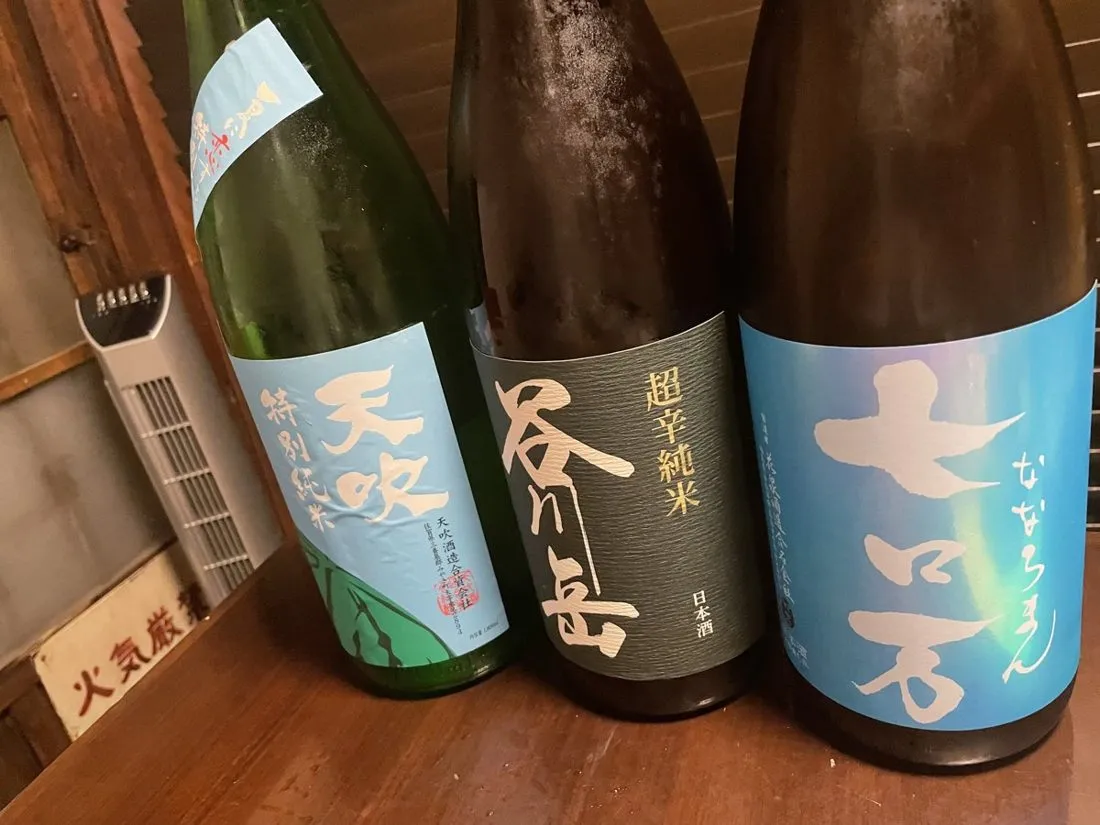 Three sake bottles standing side by side on a wooden counter