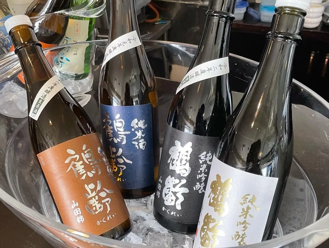 Several sake bottles chilling in an ice bucket at a bar counter